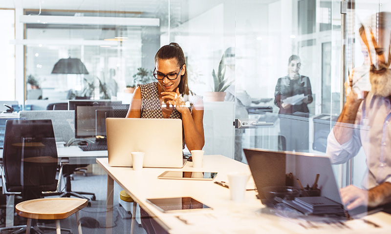 Business woman sitting at her laptop in a glass meeting room.